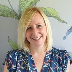 Hannah Winstanley, a white woman with blonde shoulder-length hair and a blue patterned top, smiling at the camera