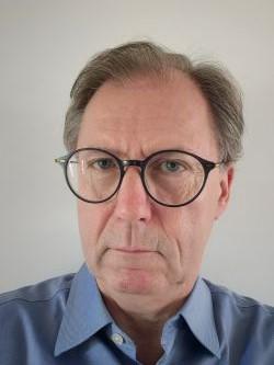 Steve Gooding, a white man, with receding grey hair and large glasses, wearing a blue shirt and looking into the camera