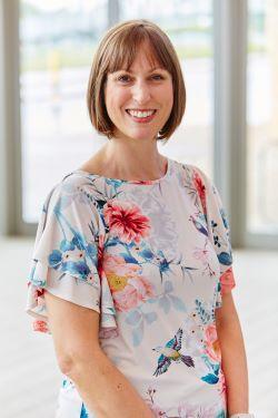 Suzy Charman, a white woman with short brown hair, wearing a flowery patterned top and smiling at the camera