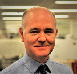 Anthony Ferguson, a bald white man wearing a light blue shirt and dark tie, looking at the camera