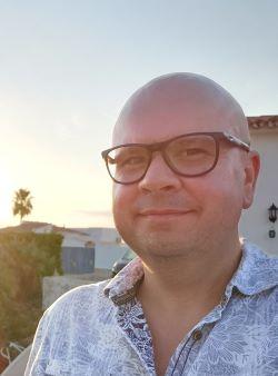 Neil Edwards, a white man, bald with large glasses, wearing a shirt and looking at the camera