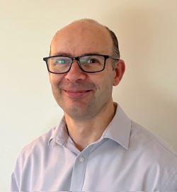 Paul Garrod, a bald white man with glasses, wearing a white shirt and smiling at the camera