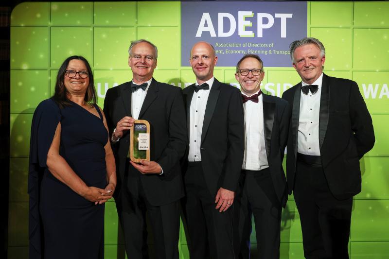 Picture shows 5 people (1 woman, 4 men) standing against a green backdrop with the ADEPT logo. One of the men is being presented with an award.