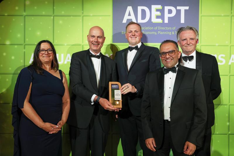 Picture shows 5 people (1 woman, 4 men) standing against a green backdrop with the ADEPT logo. One of the men is being presented with an award.