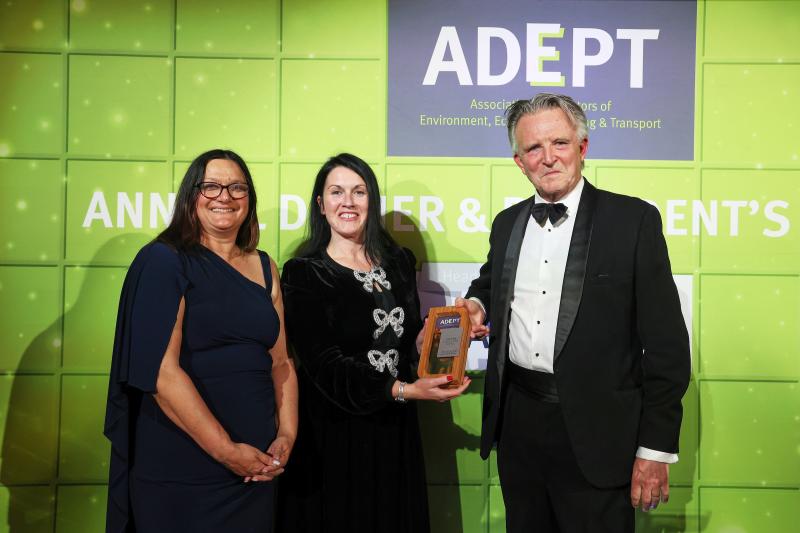 Picture shows 3 people (2 women, 1 man) standing against a green backdrop with the ADEPT logo. One of the women is being presented with an award.