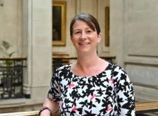 Angela Jones, a white woman in her late 40s, with shoulder-length brown hair, brown eyes, wearing a floral top and looking at the camera, leaning on a balustrade