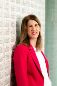 Helen Leach, a white woman in her mid-forties, with brown shoulder-length hair, wearing a bright pink jacket and white t-shirt, looking at the camera and smiling.